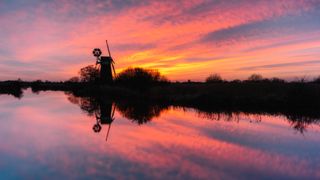 Fenland windpump next to a river at sunset with the sunset reflecting in the water