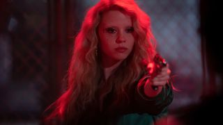 Mia Goth aims a pistol with confidence while bathed in red neon light in MaXXXine.