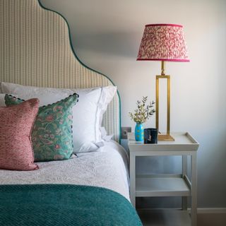 bedroom with scalloped headboard, pink cushions and teal throw