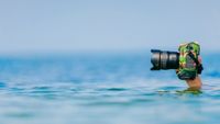 Male diver swimming under water and keeping dry and safety professional photocamera at his hand above water in ocean. Crazy photographer making photos from deep sea. Funny and dangerous hobby and job.