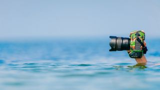 Male diver swimming under water and keeping dry and safety professional photocamera at his hand above water in ocean. Crazy photographer making photos from deep sea. Funny and dangerous hobby and job.