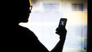 The X logo is seen on a mobile device held in the hand of a man with glasses in this illustration photo.