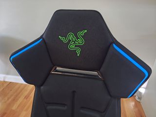The upper backrest of the chair showcasing a green embroidered Razer snake logo and blue Chroma RGB lighting strips along the shoulder wings.