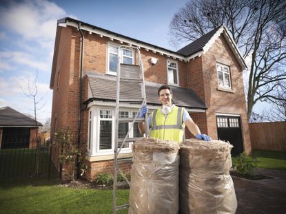 Man with loft insulation and ladder in front of house