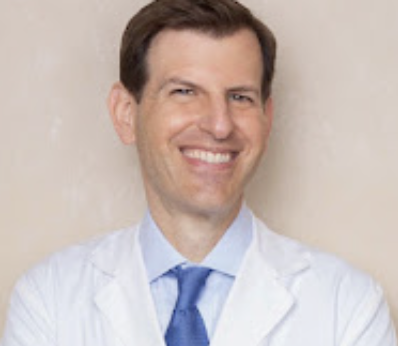a white man with brown hair wearing a shirt, tie, and white lab coat