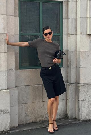 a photo showing what to wear to work in the summer with a woman wearing a gray crewneck top with black pleated shorts and black sandals