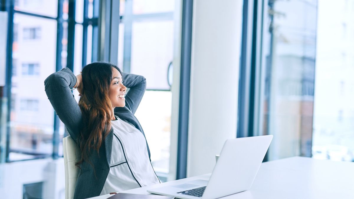 A female office worker sat back in her chair at her desk, with her arms behind her head in a relaxed pose.