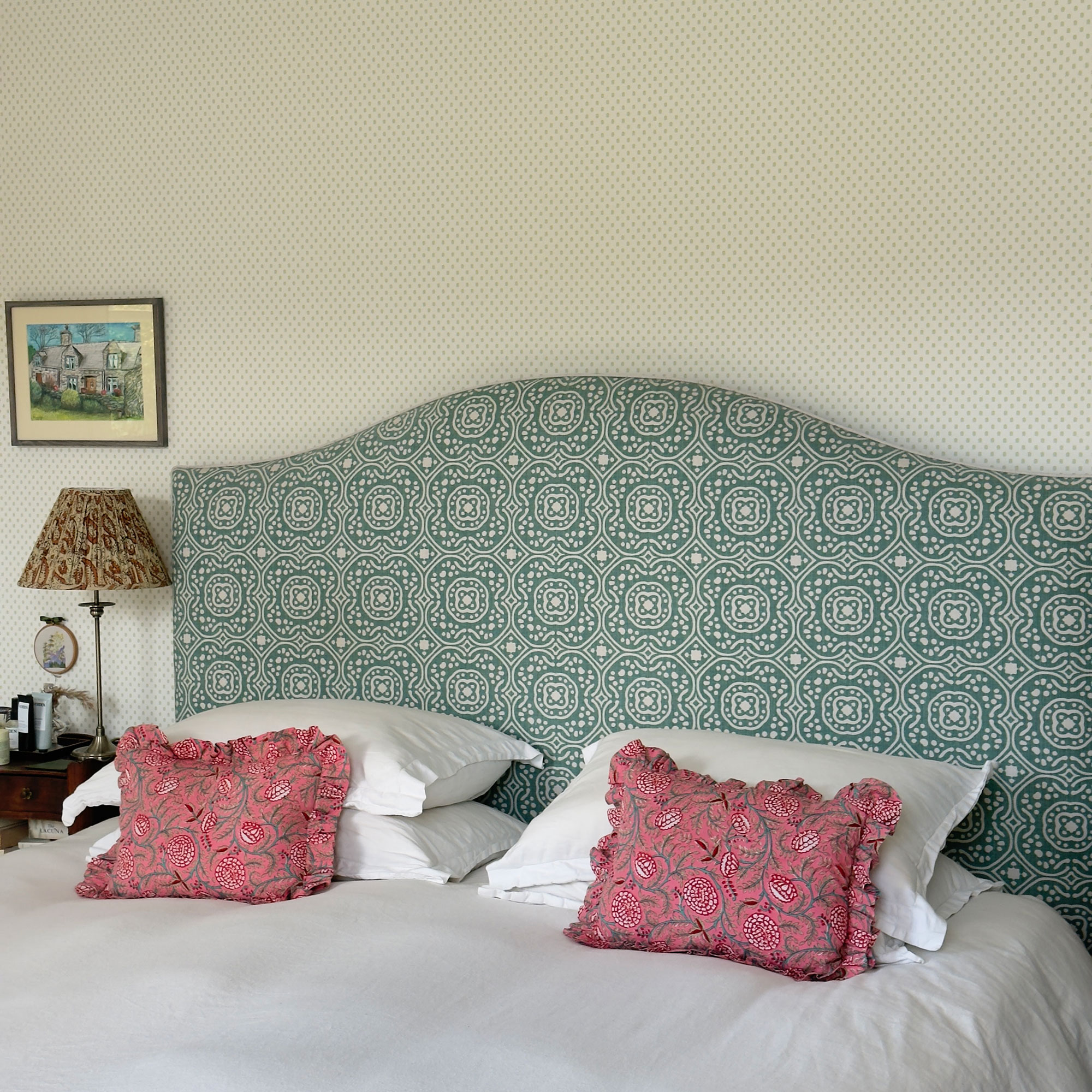 Bed with upholstered patterned green headboard and two pink floral decorative pillows