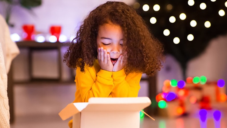 A young girl opening a present, looking surprised.