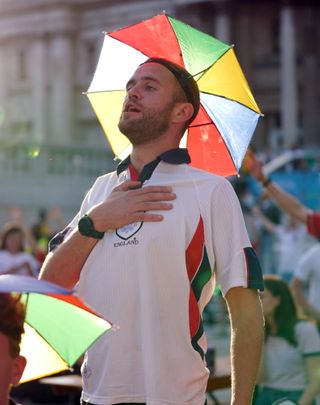 An England fan in a novelty umbrella hat sings the national anthem in Trafalgar Square