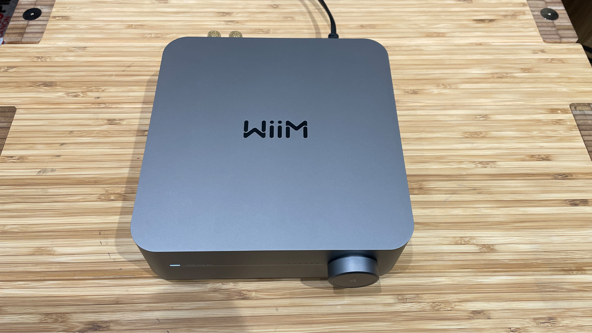 WiiM Amp Pro streaming amplifier on wooden surface, top down view showing WiiM logo