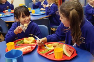 primary school kids eating school dinners off red food trays