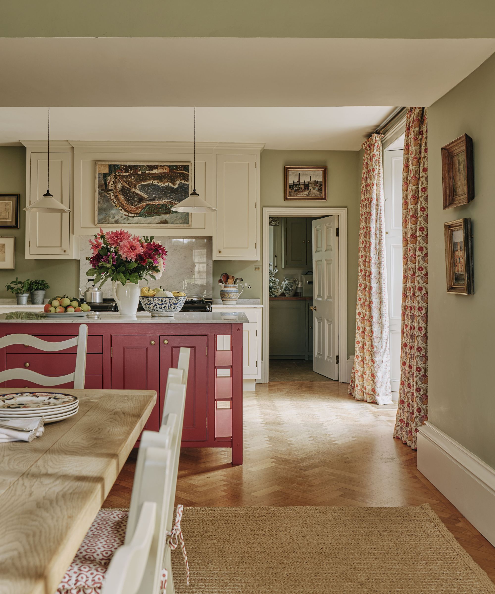 Open kitchen and dining space with a vibrant red island, wooden dining table, white cabinets, and herringbone wood floors