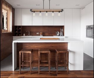 White kitchen with wood detail with central pendant light over an island; window has a venetian blind