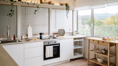 An image of a white kitchen with white cabinets and countertops and a wooden mini island to the right showing some of the things professional organizers always have in a small kitchen