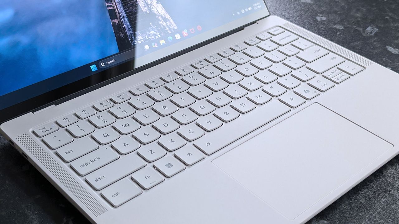 A sleek Lenovo Yoga Slim 7i Ultra (Gen 11) Aura Edition laptop on a dark surface, viewed at an angle. The screen displays a blurred image, with a focus on the keyboard and touchpad.