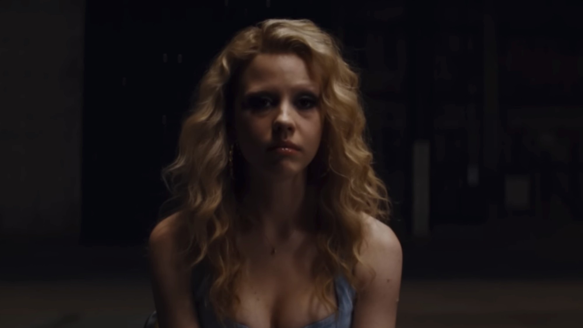 Mia Goth looking right into the camera in a darkened room