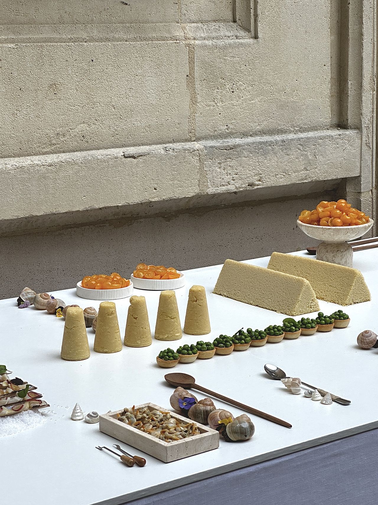 A series of couscous food sculptures, snails, shells, and tomatoes is beautifully positioned on a white cloth table along with silver and wooden cutlery.
