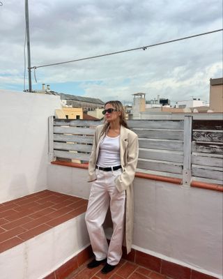 Woman wearing ecru jeans with a white tank top and a beige trench coat.