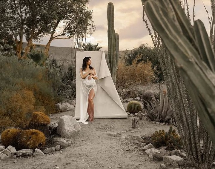 A woman standing against a paper backdrop in a desert