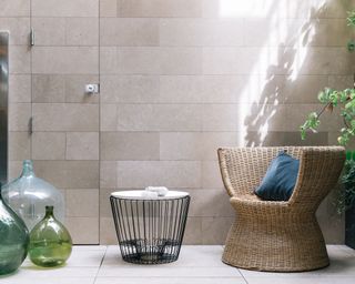 A small courtyard garden with tiles on the wall and floor and a wicker armchair.