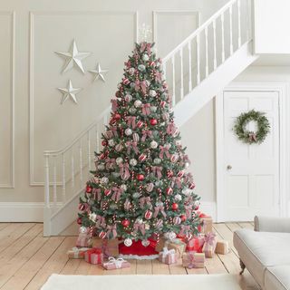 A realistic looking artificial Christmas tree decorated in red and white baubles in a wooden floored living room