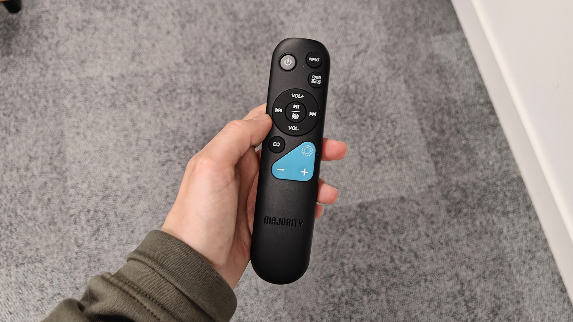 Majority Bowfell Halo Atmos soundbar system remote control held in hand above grey carpet