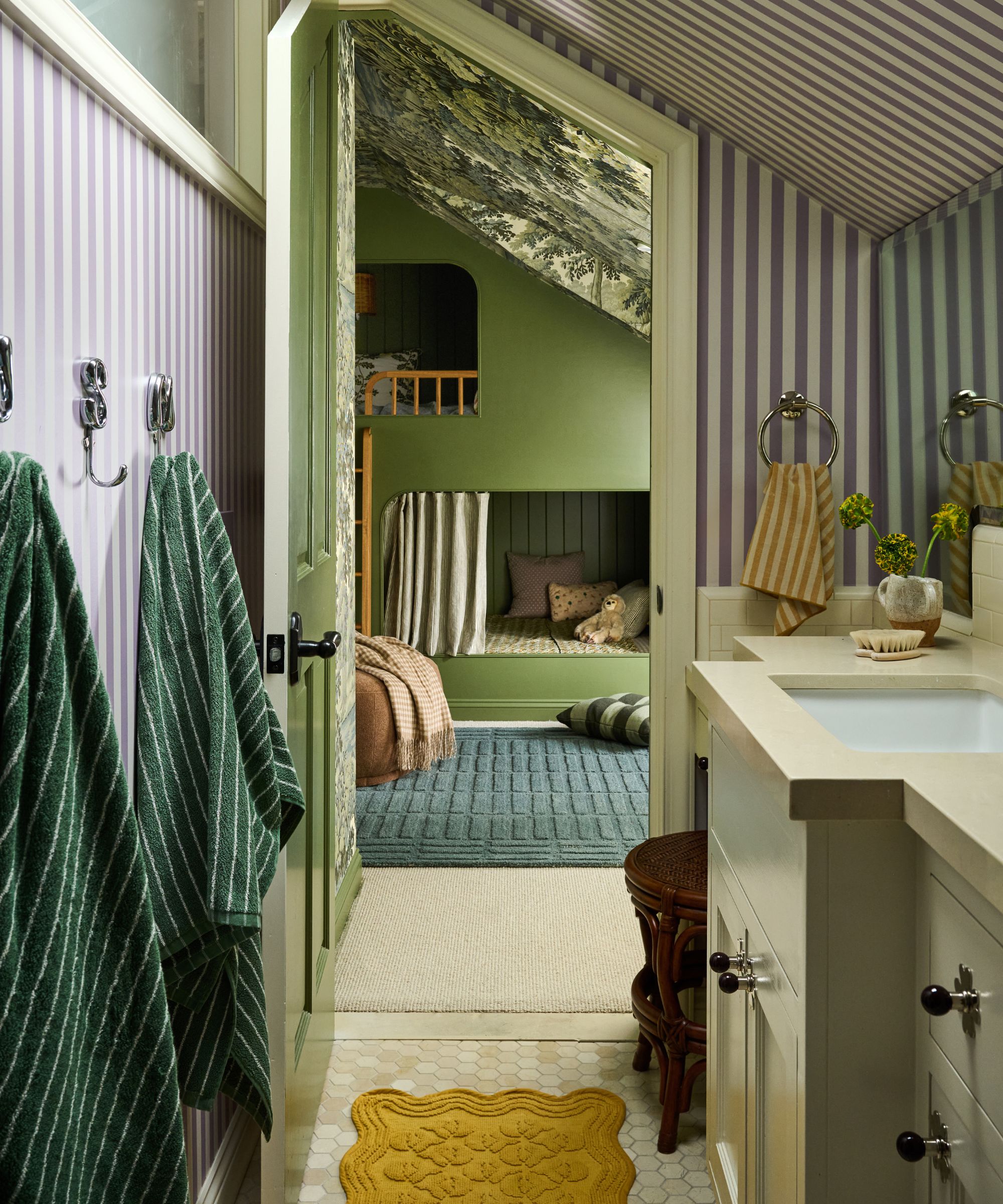 a kids bathroom wrapped in striped wallpaper with angled ceiling and a soft neutral vanity
