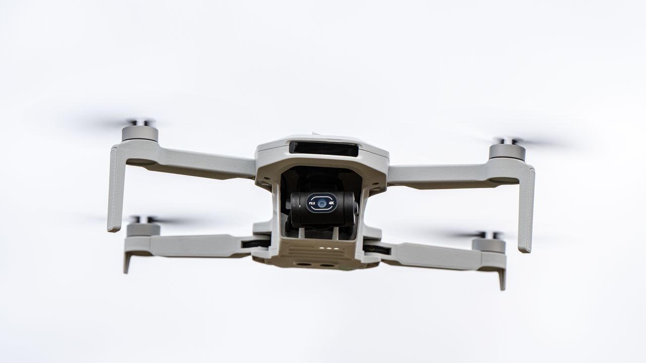 A white drone with black camera is in flight.