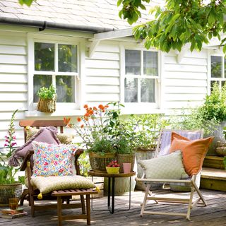 Two wooden deckchairs on decking surrounded by pots of flowering plants