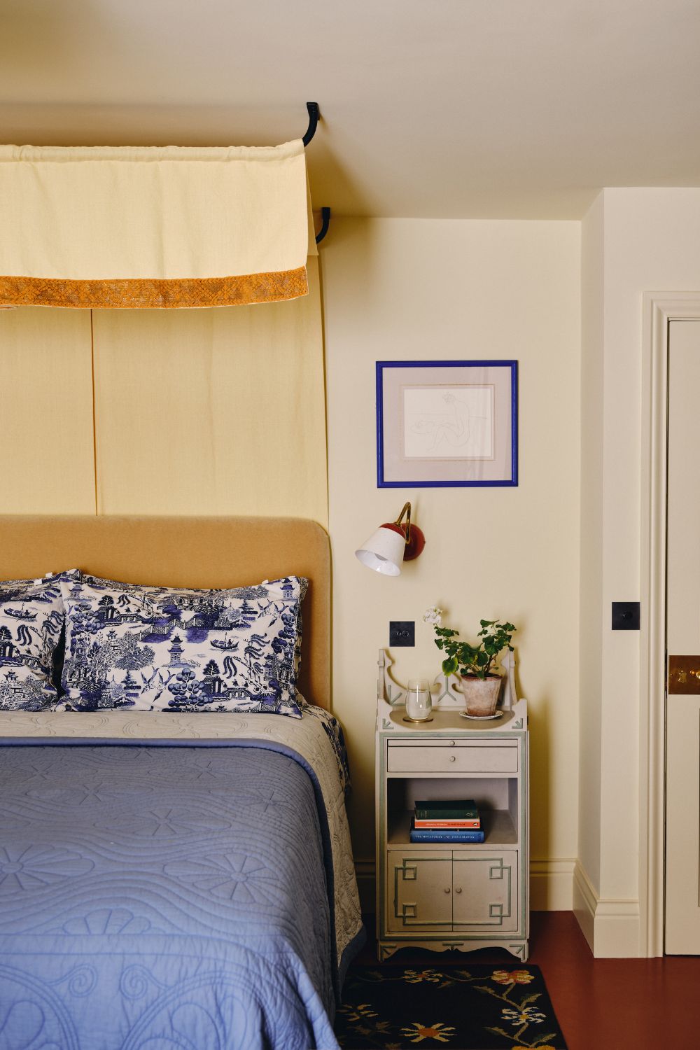 soft butter yellow bedroom with a yellow bed canopy, ochre velvet headboard and blue toile bed linen with a vintage nightstand