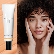 A woman with glowing skin and freckles next to a bottle of skin tint with SPF. 