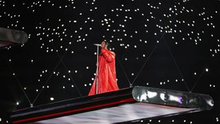 Rihanna lowers onto the stage in her bright red dress at the Super Bowl LVII Halftime Show. 