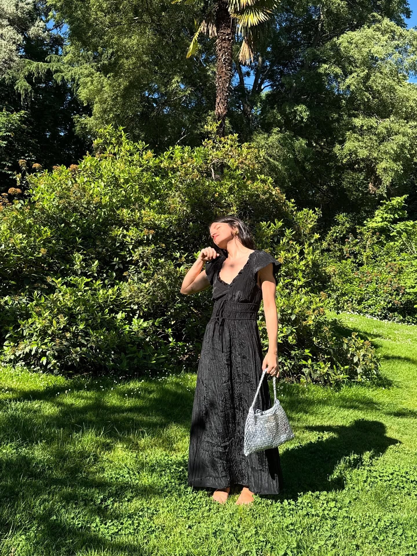 Woman wears black crinkle dress, crochet bag and sandals