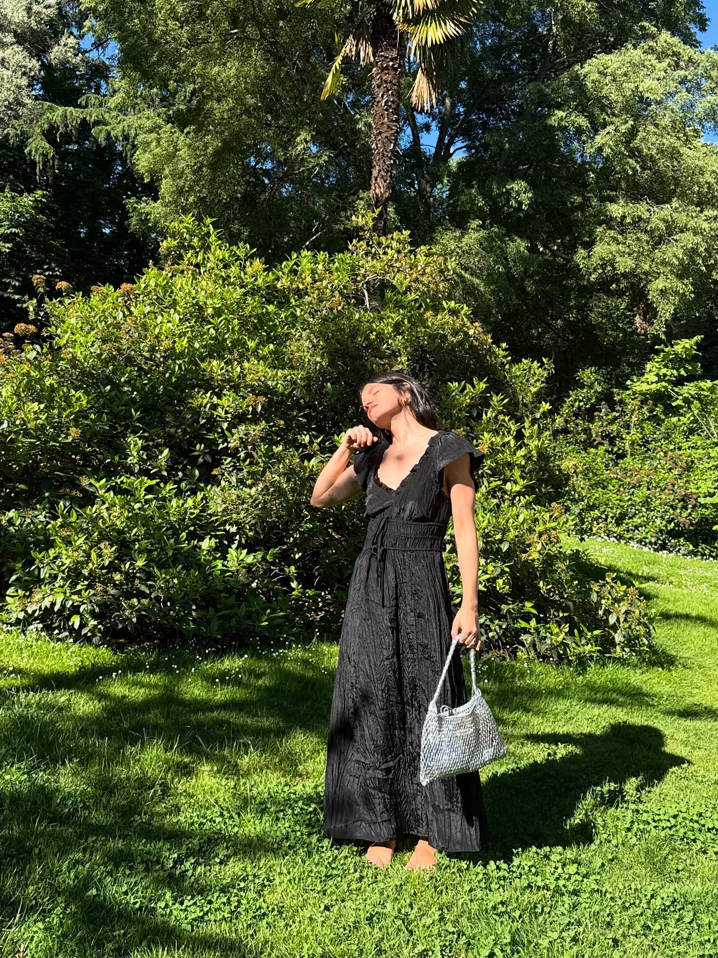Woman wears black crinkle dress, crochet bag and sandals