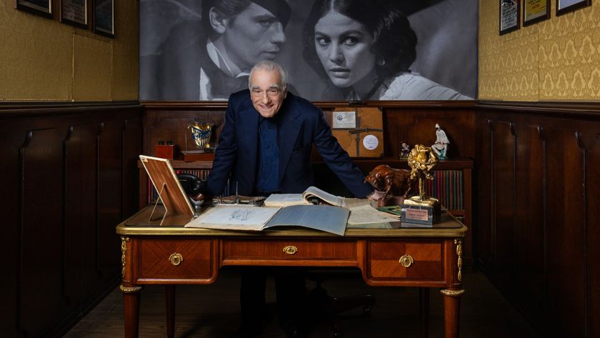 Legendary film director Martin Scorsese is seated behind a large wooden desk in a richly decorated, wood-paneled office with a classic movie poster visible on the wall behind him.