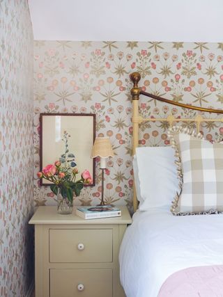 cast iron bedhead with floral wallpaper and artwork checked cushion and pink bedspread