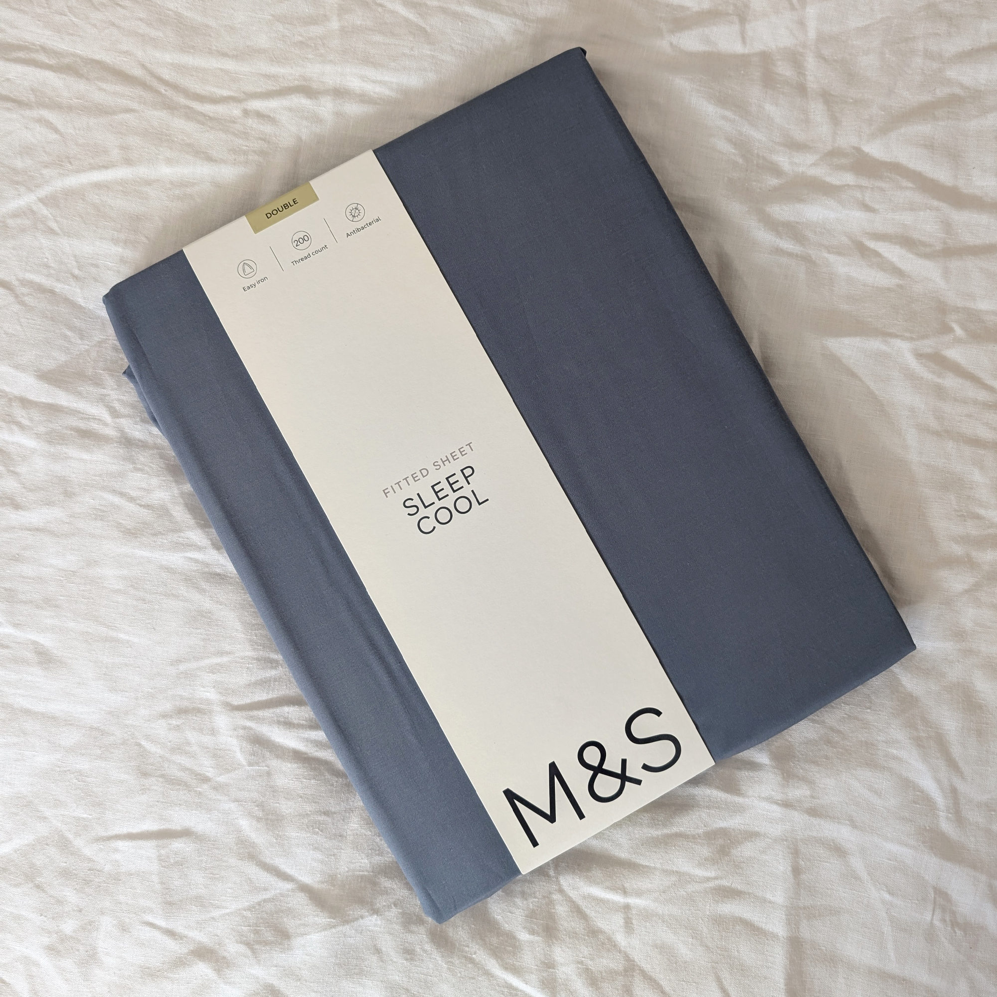 M&amp;amp;S Stay Cool Lyocell Rich Fitted Sheet in blue on a bed with white linen bedding