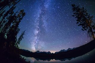 Milky Way stretches up into the sky with lake below reflecting the stars above.