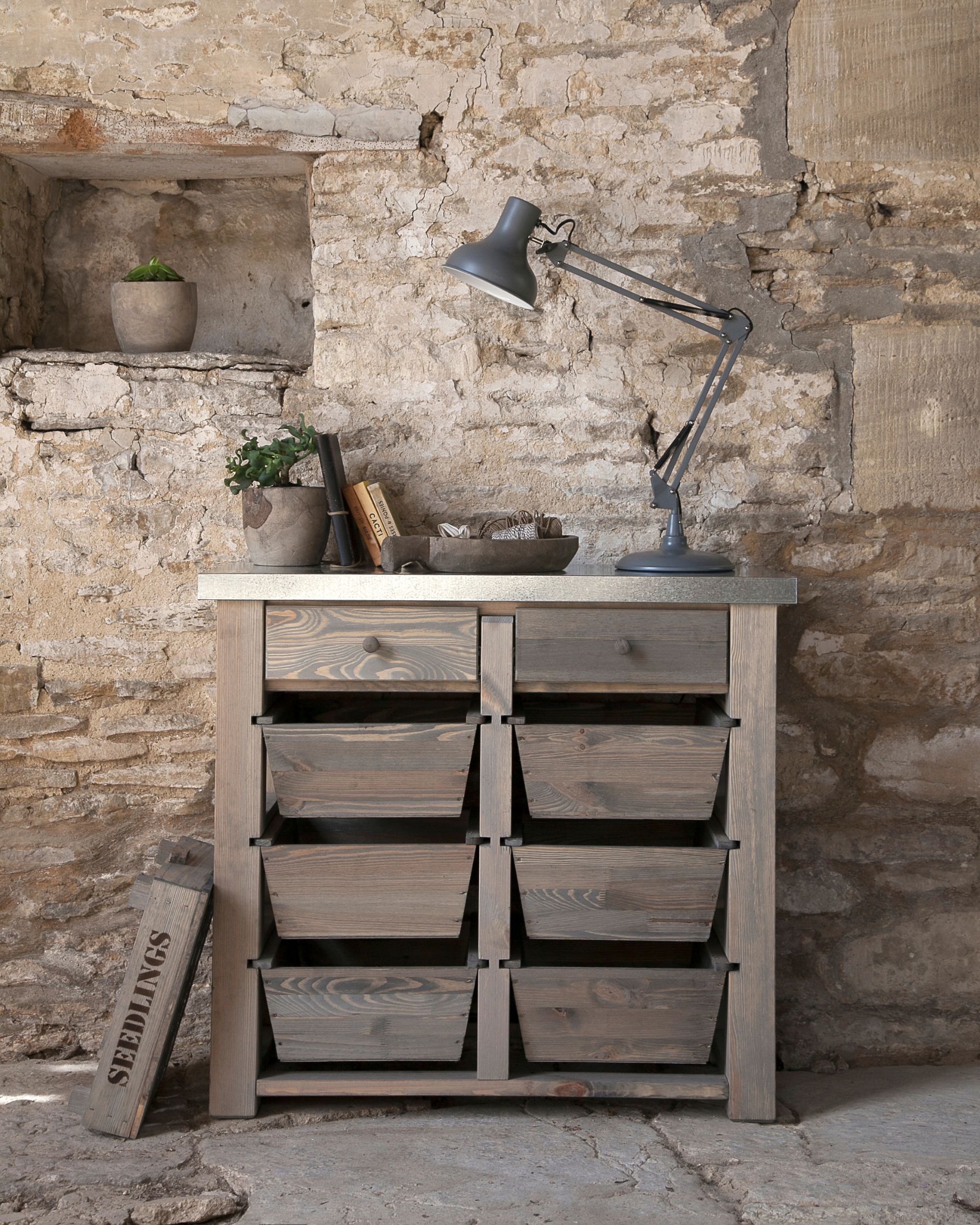 Wooden storage unit with a metal worktop in front of a stone wall.