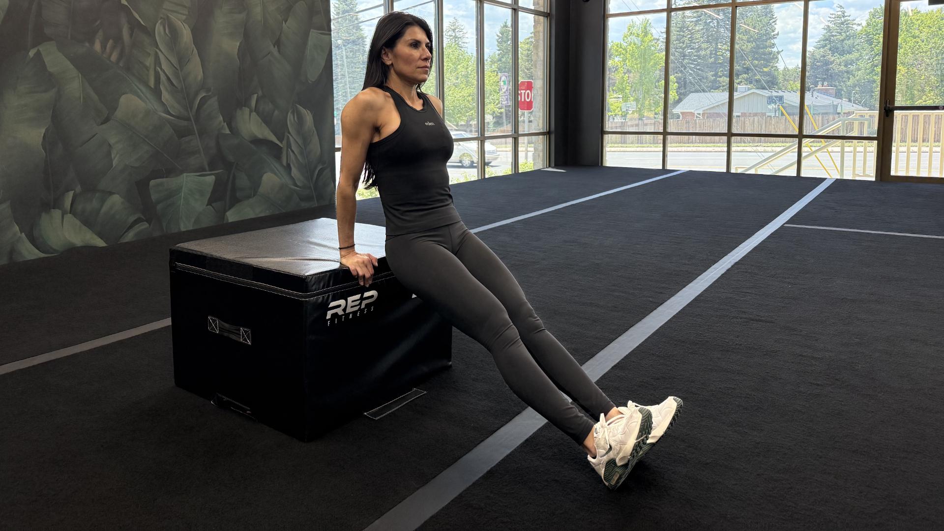 Woman exercising in empty gym space, performing a triceps dip with a plyo box