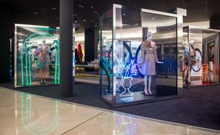 A store with mannequins displayed in glasses cases with neon lights in them.