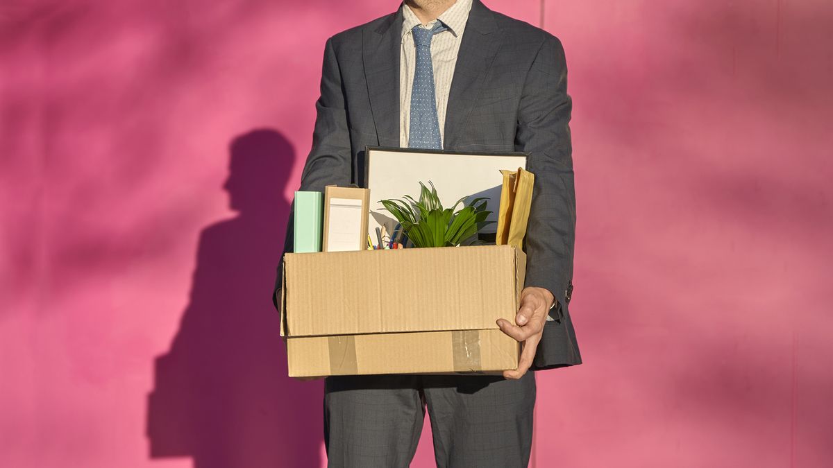 A businessman holding a cardboard box with his desk contents inside, indicating that he&#039;s lost his job