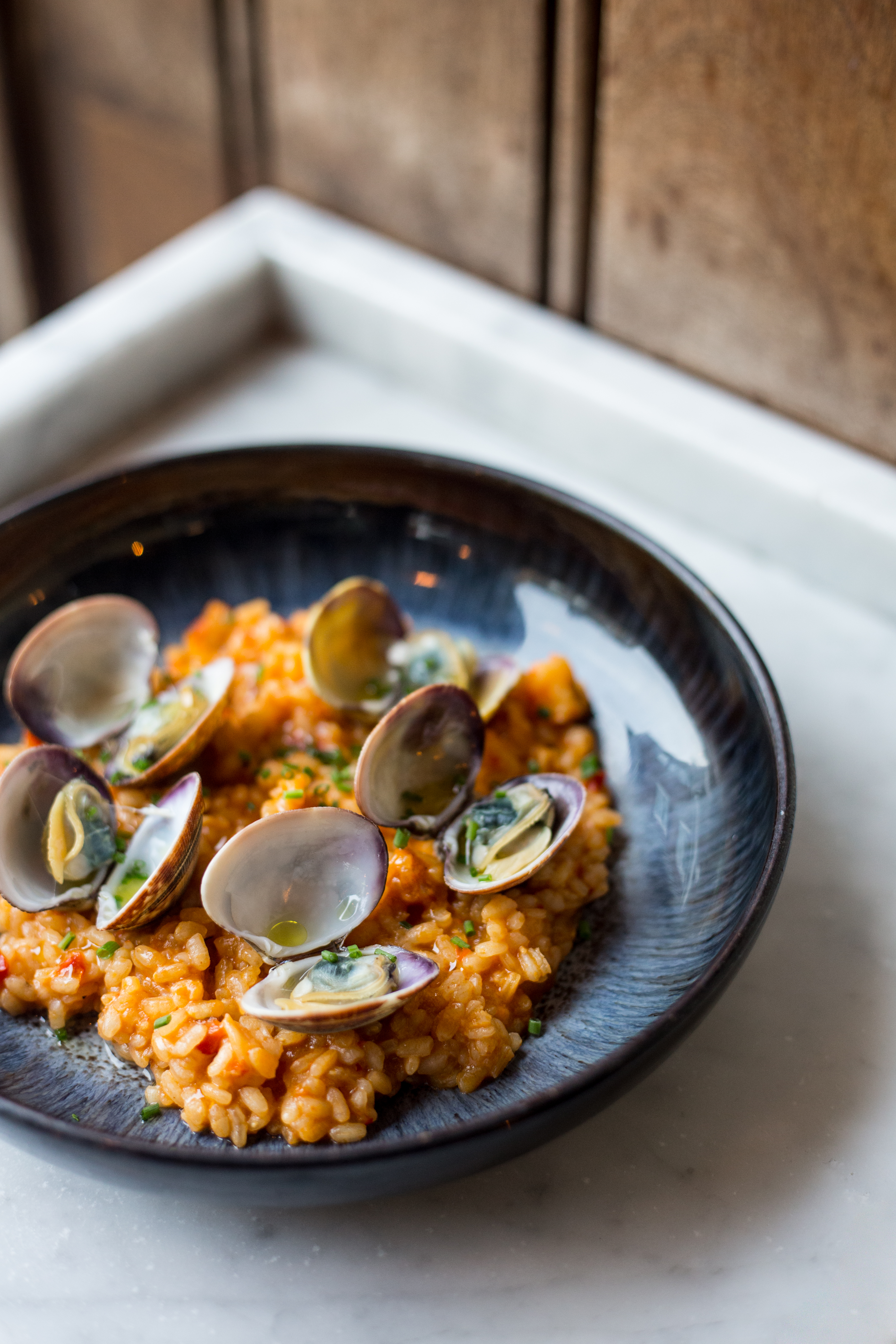 A ceramic bowl filled with clam rice sits atop a marble countertop.