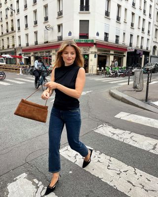 Woman in Paris wearing cropped jeans, kitten heels, a black top, and a brown suede bag