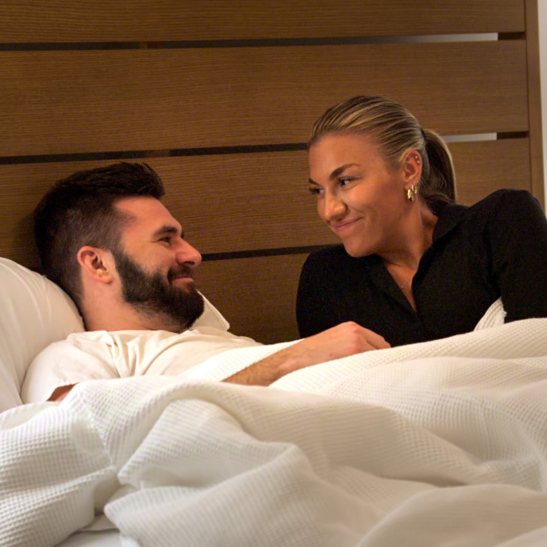 connor and bri lay in bed together and smile looking at one another in a still from love is blind season 10