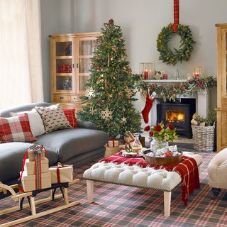 A Christmas themed living room with tartan carpet, a grey sofa and cream footstool
