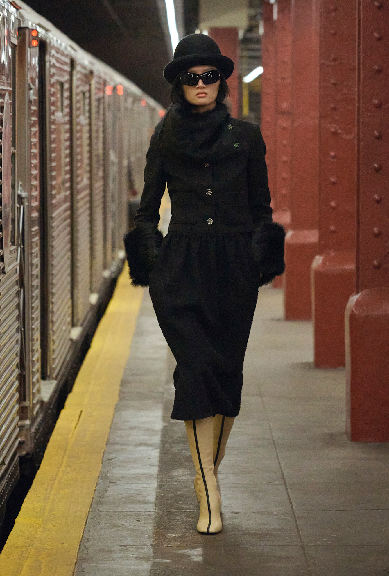 a model at chanel pre-fall 2026 wearing a black lady jacket, black fur scarf, black skirt, black hat, and tan boots