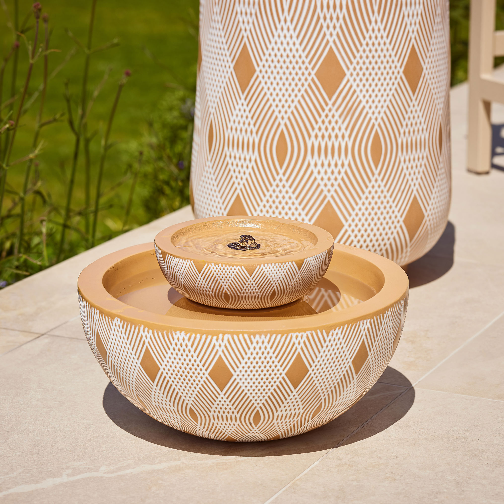Terracotta water feature on a white patio with beige outdoor dining set
