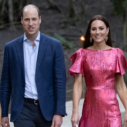 Prince William wears a navy suit with a light blue shirt and Kate Middleton wears a metallic pink dress
